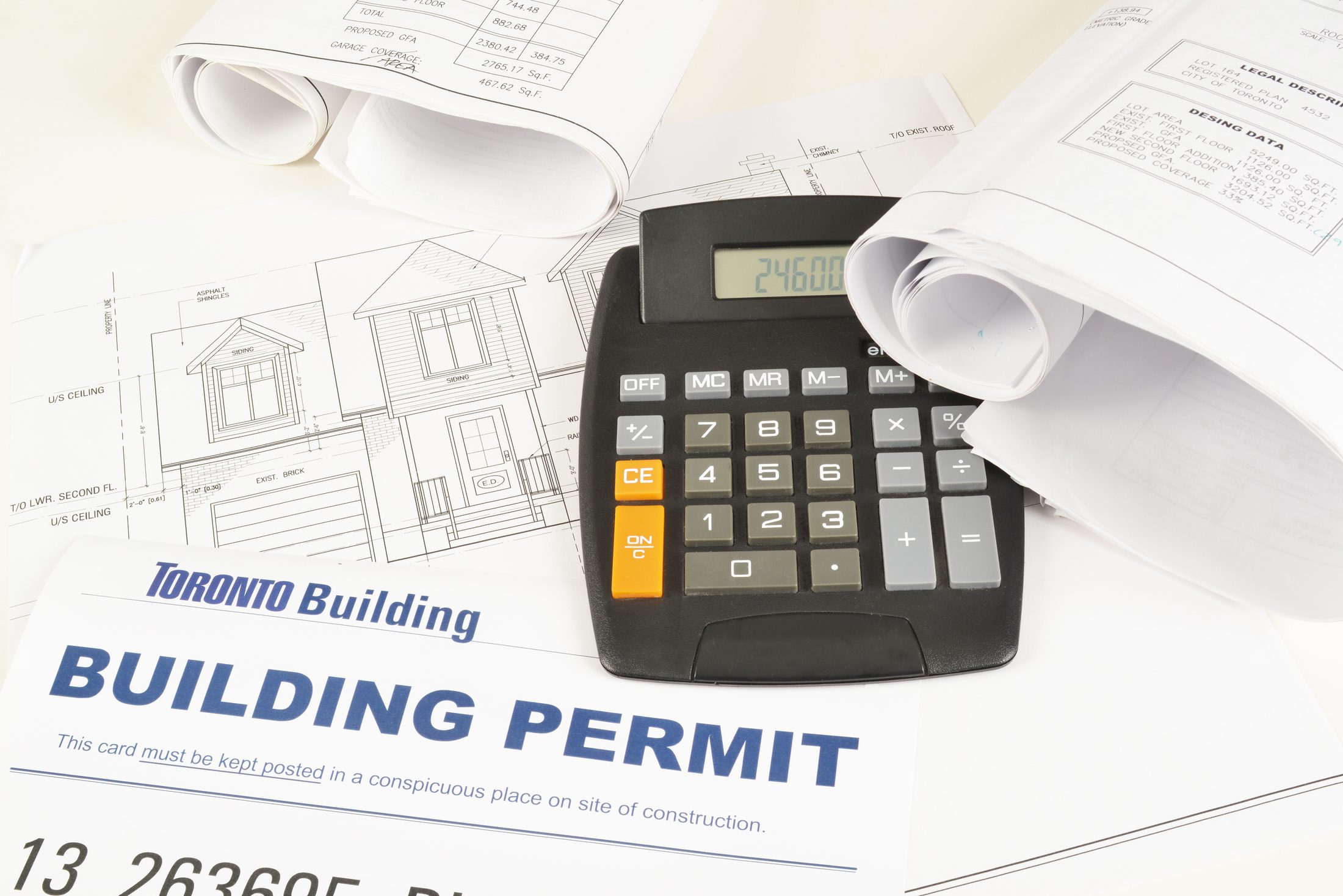 A calculator resting on building permit paperwork and architectural elevation drawings